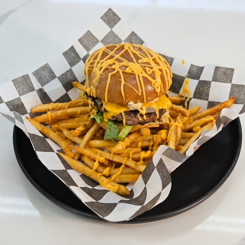 Cheesy burger with lettuce and onions, served with cheese-drizzled fries in checkered paper.