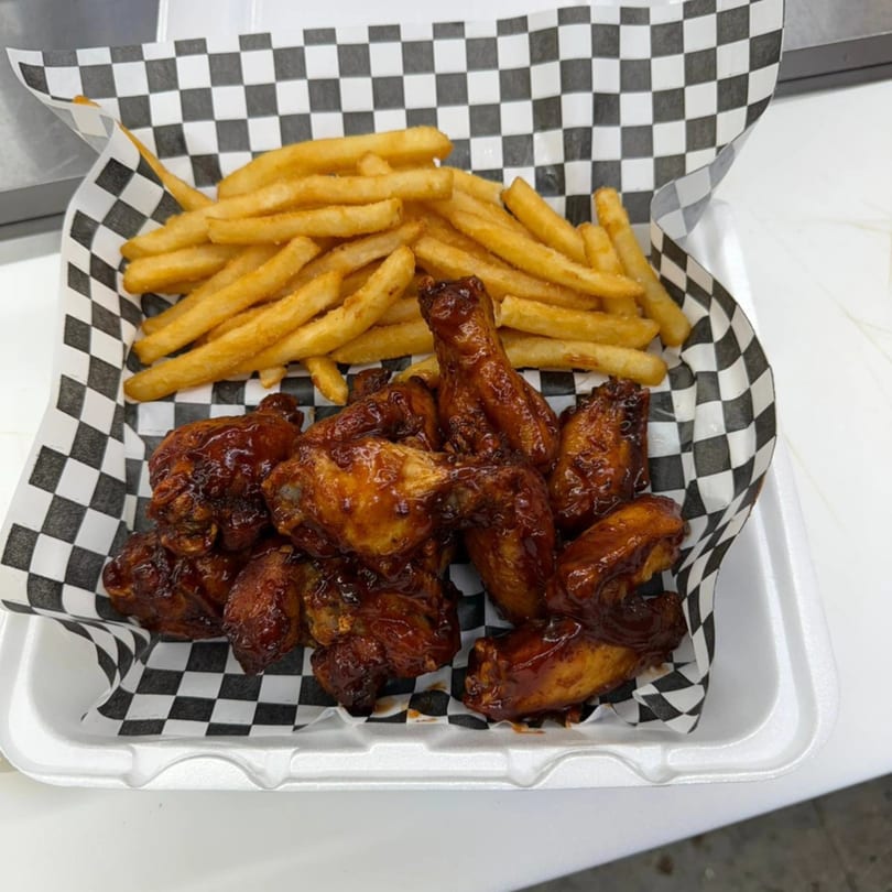 BBQ chicken wings and golden french fries served in a white styrofoam container with checkered paper.